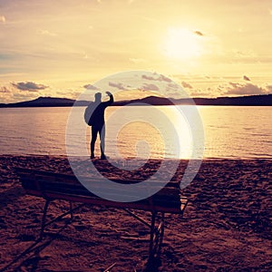 Alone traveler with backpack. Man on sea beach at wooden bench, cold sunny autumn evening