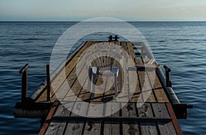 Alone white plastic chair sits on wooden dock by the blue calm sea, pier on shore, coast of Lake Baikal. Clear horizon