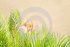Alone woman applying sunscreen on skin sitting under palm tree branches. Female relaxation on the sand of the beach at summer