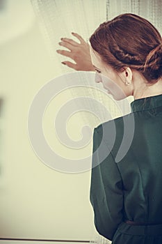 Alone woman looking through window waiting