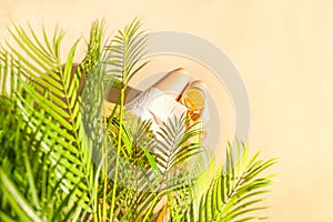 Alone woman sitting under palm tree branches with glass of water with piece orange. Female relaxation on the sand of the beach