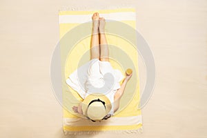 Alone woman in straw hat and dress sitting on yellow beach towel and drinking orange juice. summer. Top, aerial view.