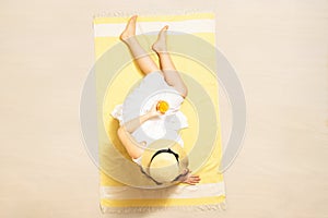 Alone woman in straw hat and dress sitting on yellow beach towel and drinking orange juice. summer. Top, aerial view.