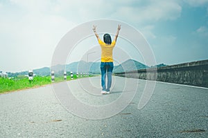 Alone woman traveler or backpacker walking along countryside road along side with reservoir, she raise hands over head.