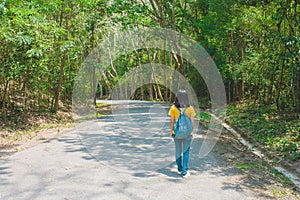 Alone woman traveller or backpacker walking along contryside road among green trees.