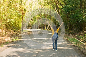 Alone woman traveller or backpacker walking along contryside road among green trees, she has feeling happiness.