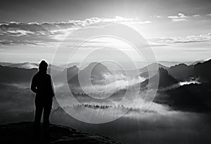 Alone young girl tourist feast autumn daybreak on the sharp corner of sandstone rock and watch over misty valley to Sun.