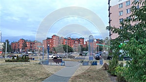 Along the city street are red brick buildings with metal roofs, trees, lampposts and parked cars. Nearby are paved sidewalks and b