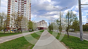 Along the city street are residential buildings with balconies, parking lot, trees, lampposts and parked cars. Nearby are paved dr