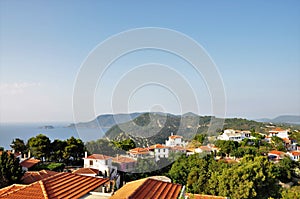 Alonissos island with red roofs, green trees, hills and the sea.