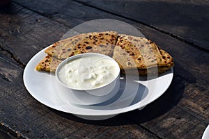 Aloo paratha and curd for breakfast placed on wooden board