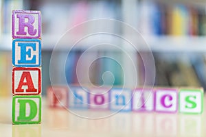 Alphabet blocks spelling the words read and phonics in front of a bookshelf