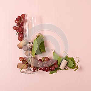 Alphabet. Letter L made of wineglasses with rose and white wine, grapes, leaves and corks lying on pink background. Wine