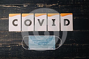 Alphabet letters cards make inscription COVID and medical gauze mask on black background. Coronavirus 2019-ncov, selfisolation photo