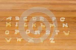 Alphabet pasta placed in alphabetical order on bamboo cutting board