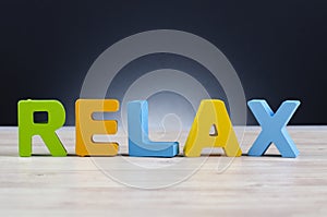 Alphabet word RELAX on wooden desk over dark background