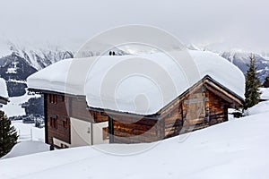 Alpine chalet sunk in deep snow in winter with thick snow on roof i