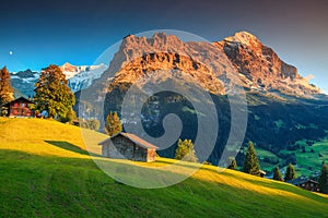 Alpine chalets with green fields and high mountains at sunset