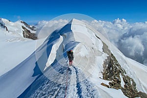 Alpine climber on sharp knife-edged snow mountain ridge