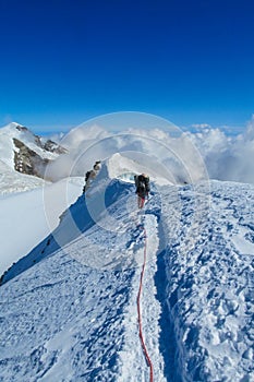 Alpine climber on sharp knife-edged snow mountain ridge
