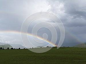 Alpine landscape with beautiful rainbow. Mountains, meadows and pastures with sunbow.