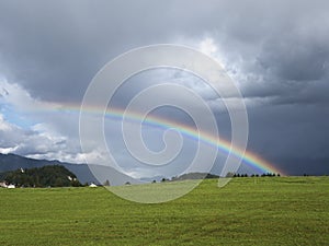 Alpine landscape with beautiful rainbow. Mountains, meadows and pastures with sunbow.