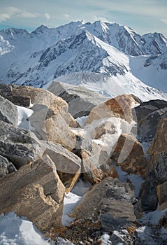 Alpine landscape with rocks at the front, peaks covered by snow and clouds, beautiful colors at the top of a glacier