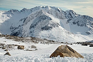 Alpine landscape with rocks at the front, peaks covered by snow and clouds, beautiful colors at the top of a glacier