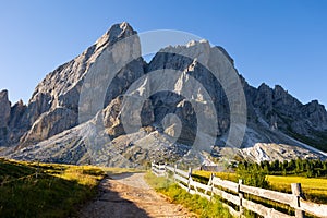 Alpine meadow with wooden-railed trail leading to Munt de Fornella in Dolomites photo