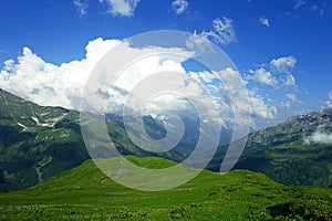 Alpine meadows, lake, mountains and lots of white clouds with beautiful summer landscape