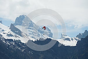 Alpine peaks covered with snow landscape in early spring with a para-glider  with red glide flying above.