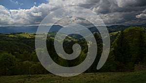 The alpine ridges of the Carpathian Mountains are surrounded by centuries-old forests on the background of the blue sky with white