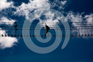 Alpine rope suspension bridge with a person against blue sky