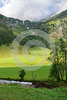 Alpine valley and waterfall with green grass and mountains in the clouds