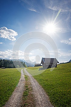 Alpine walkway near Gerold, spring landscape with huts and bright sun, blue sky with clouds