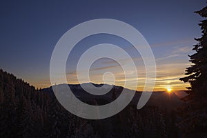 Alpine winter scenery with foggy valleys at the base of Piatra Craiului and Postavaru mountains at sunset