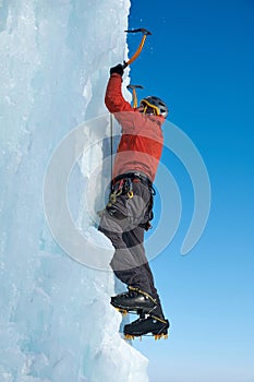 Alpinist man with ice tools axe climbing a large wall of ice. Outdoor Sports Portrait