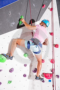 Alpinist practicing indoor rock climbing in special equipment