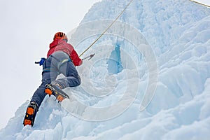 Alpinist woman with ice tools axe in orange helmet climbing a l