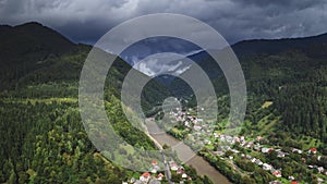 Alps mountain village under storm clouds sky. Aerial flight over countryside houses along the river