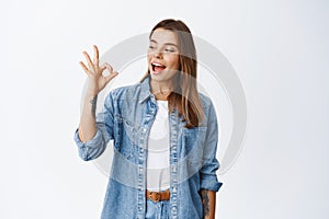 Alright. Smiling cute girl showing okay sign and say yes, approve something good, like and agree, standing pleased photo