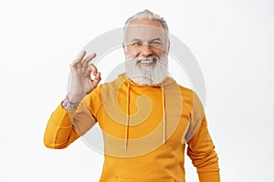 Alright. Smiling hipster senior showing OK okay agree gesture, looking happy and satisfied, give approval, praise