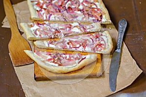 Alsatian tart flambÃ© or Flammkuchen with bacon and onions on a dark table.