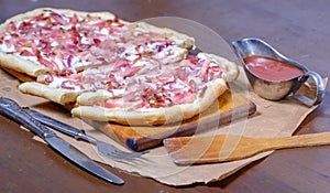 Alsatian tart flambÃ© or Flammkuchen with bacon and onions on a dark table.