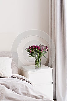 Alstroemeria flowers in a glass vase on a bedside table of white color in a bedroom