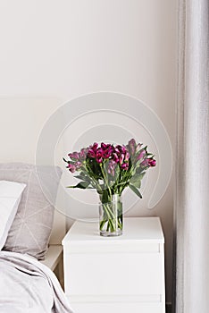 Alstroemeria flowers in a vase on a white bedside table. Simple and cozy bedroom decor