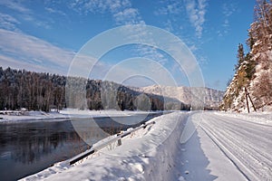 Altai winter road and river Biya in winter season. Banks of river are covered by ice and snow