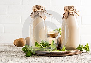Alterative potato vegetable milk in two glass bottles on a tray against a white brick wall. the concept of a healthy vegetarian