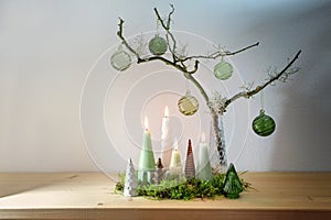 Alternative advent wreath decoration with four different candles, small artificial Christmas trees and green glass baubles on a