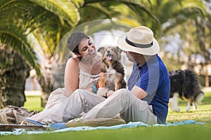 Alternative animal love family couple play with young puppy shetland collie on the meadow in a park - playful people with dogs